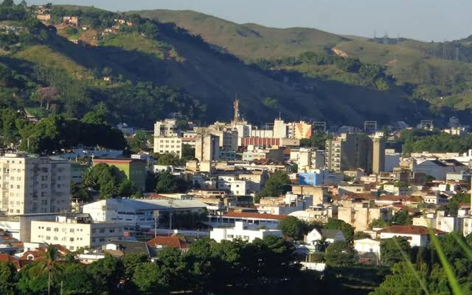 Vista da área urbana de Barra do Piraí, no Rio de Janeiro, com prédios, o rio e os morros ao fundo.